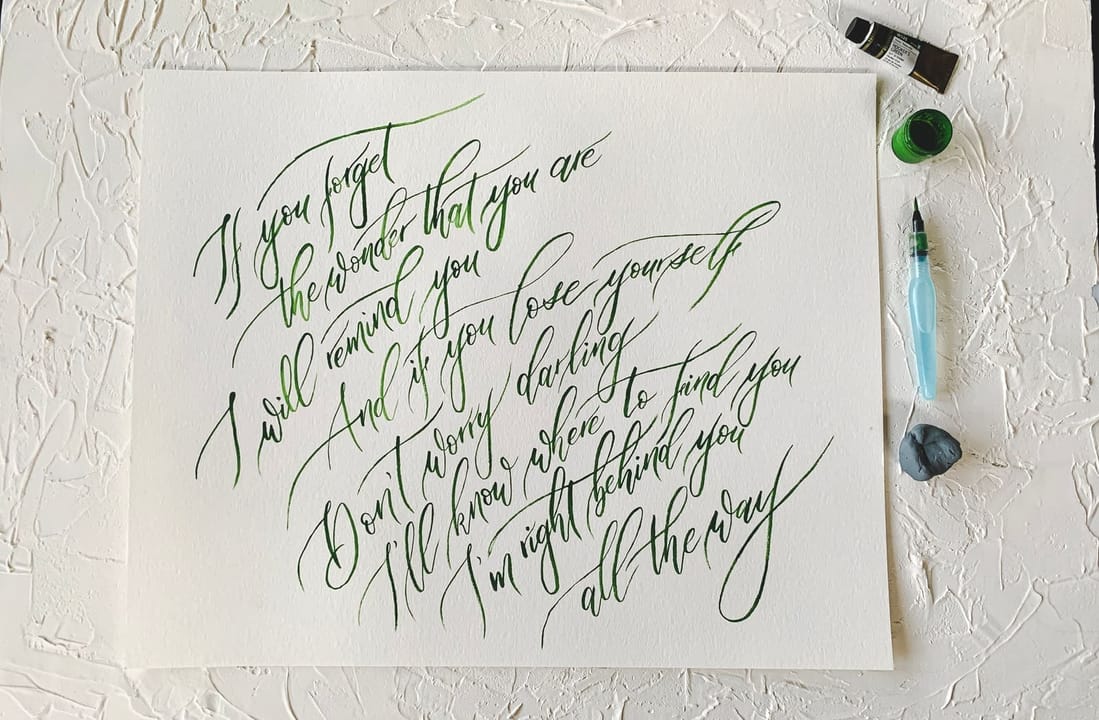 A large flourished calligraphy piece in green ink, alongside gouache and a water brush