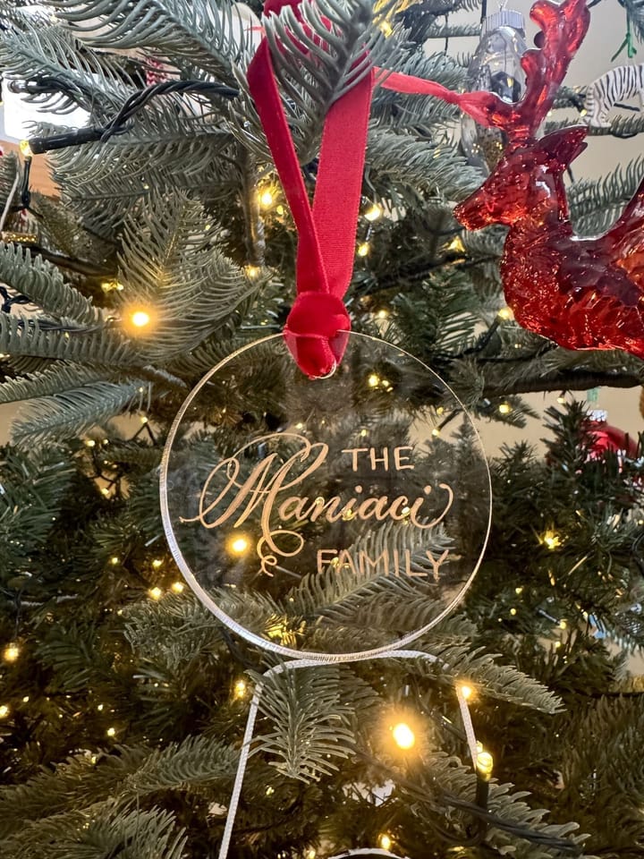 Gold hand-lettered family ornament hanging on a lit Christmas tree