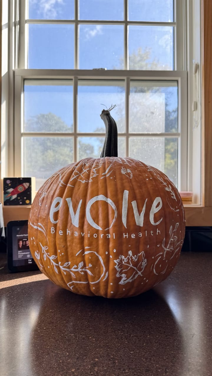 A pumpkin hand-lettered with a local business's evolve Behavioral Health logo, surrounded by painted autumn leaves and acorns