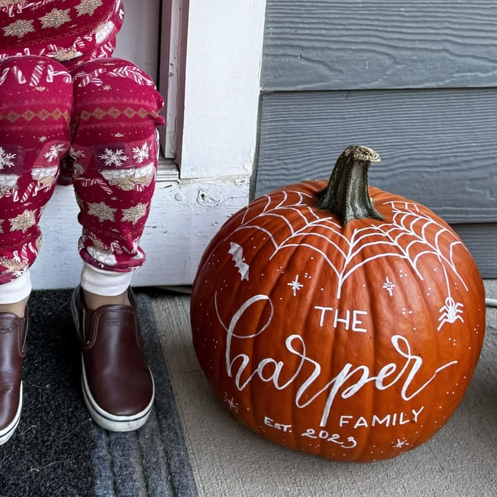 A hand-lettered pumpkin with a painted spiderweb and family name