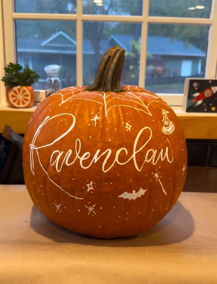 A hand-lettered pumpkin reading Ravenclaw with painted stars and a sorting hat