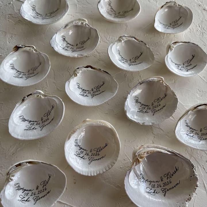 A spread of hand-lettered clam shell wedding favors with names and a wedding date