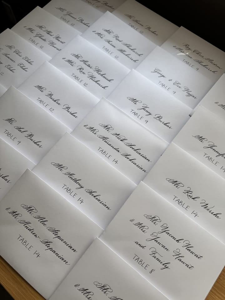 A wide flat-lay of hand-lettered escort card envelopes sorted by table
