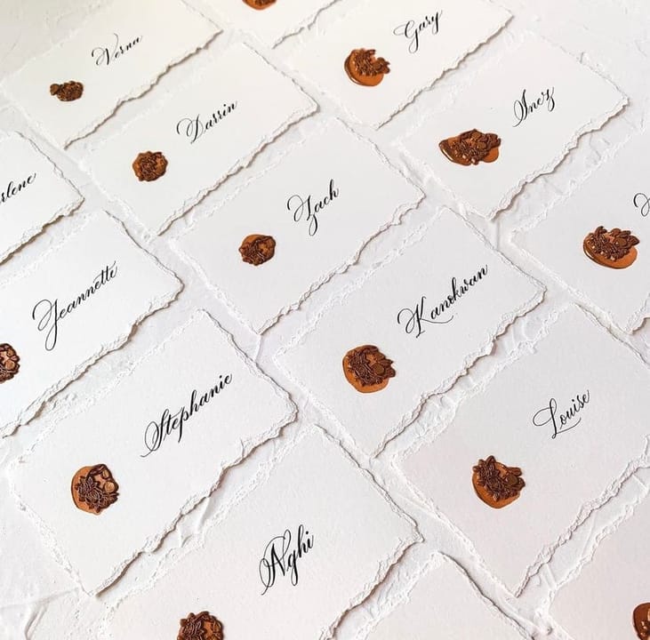 A full layout of place cards on deckled paper, each finished with a copper wax seal