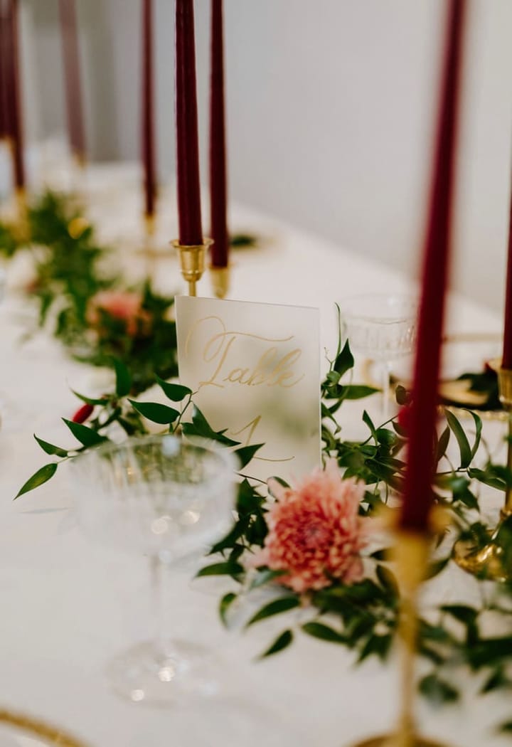 Gold hand-lettered table number card on frosted acrylic among floral place settings