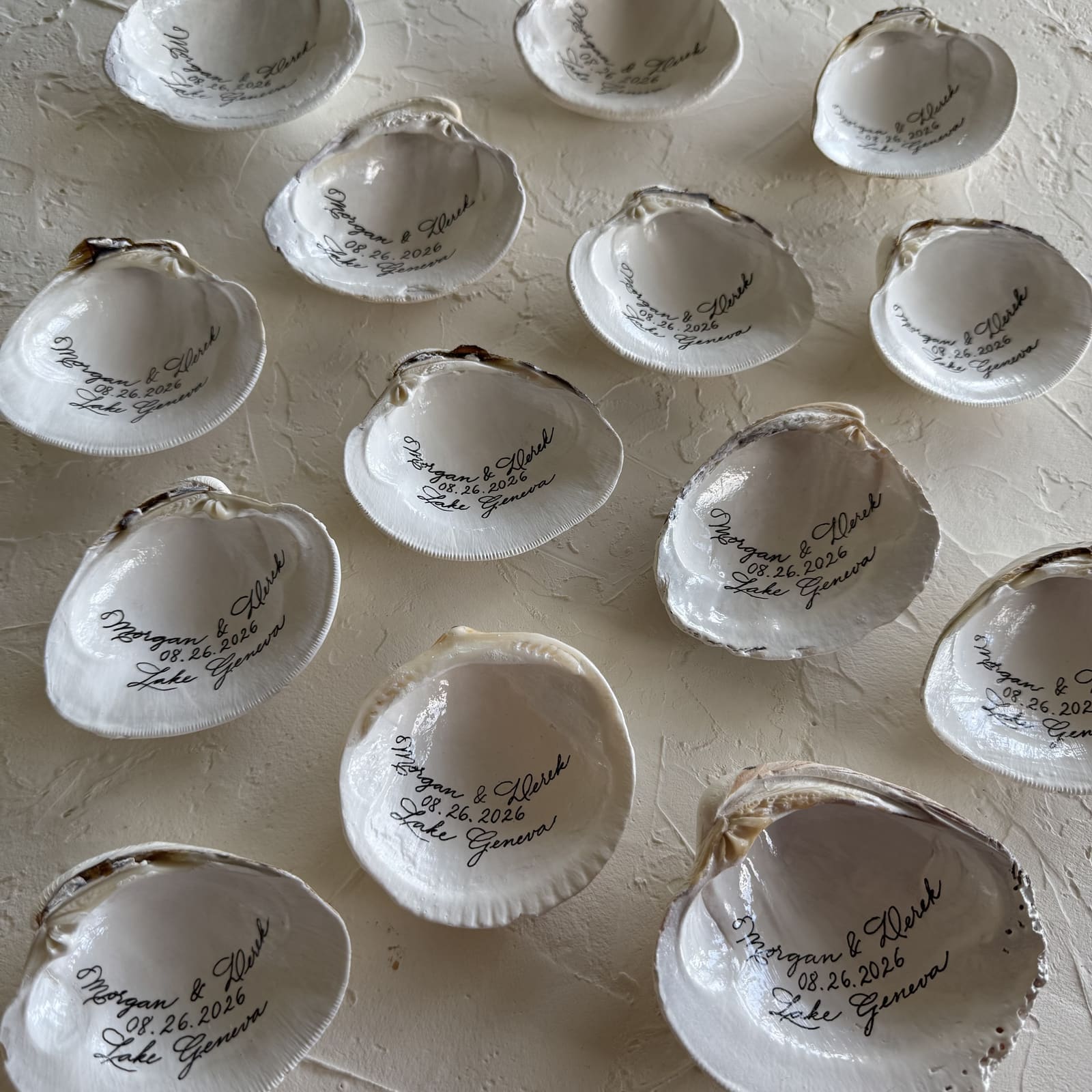 A spread of hand-lettered clam shell wedding favors with names and a wedding date